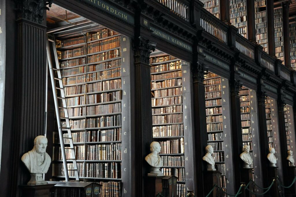 Old text library with many old books along the shelves and busts of famous authors and leaders set up at each case.