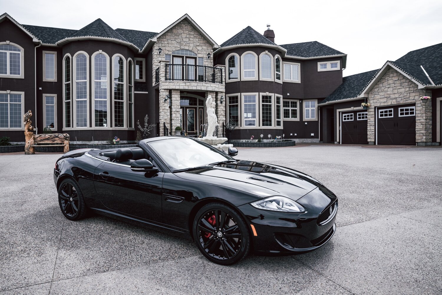 Black luxury car parked in front of a mansion.